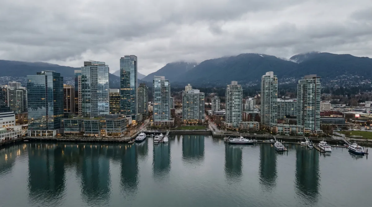 Glass condo towers along Vancouver's waterfront with North Shore mountains under overcast sky